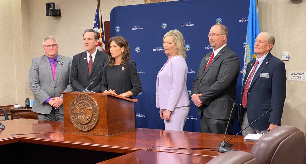 Senator Jim Bolin (far right) assumes the proper position during a Kristi Noem press conference. Photo from Governor Kristi Noem's Twitter, 2020.03.09.