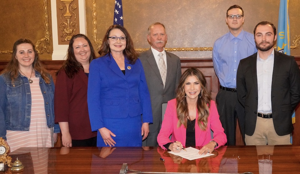 Logan Manhart violated South Dakota election-requirements last year; now he works in the elections office and smirks as Governor Noem signs updates to South Dakota's voter residency requirement. Photo from Governor's Office, 2023.03.21.