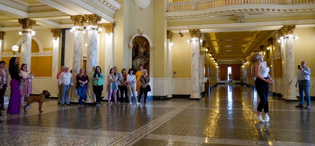 Governor Noem and her dog and other loyal staff watch press secretary Amelia Joy twirl her baton in the Capitol Rotunda, tweeted by Gov. Kristi Noem 2023.04.19.
